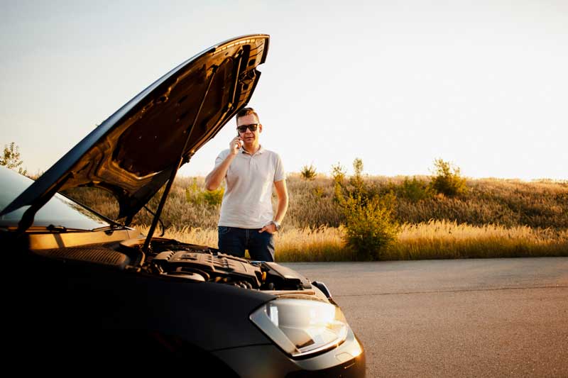 Regionaler Autoankauf-Service – Ihr Fahrzeug in besten Händen Eine Person in einem weißen Hemd steht neben einem Auto mit offener Motorhaube und spricht am Telefon vor einem Sonnenuntergangshorizont.